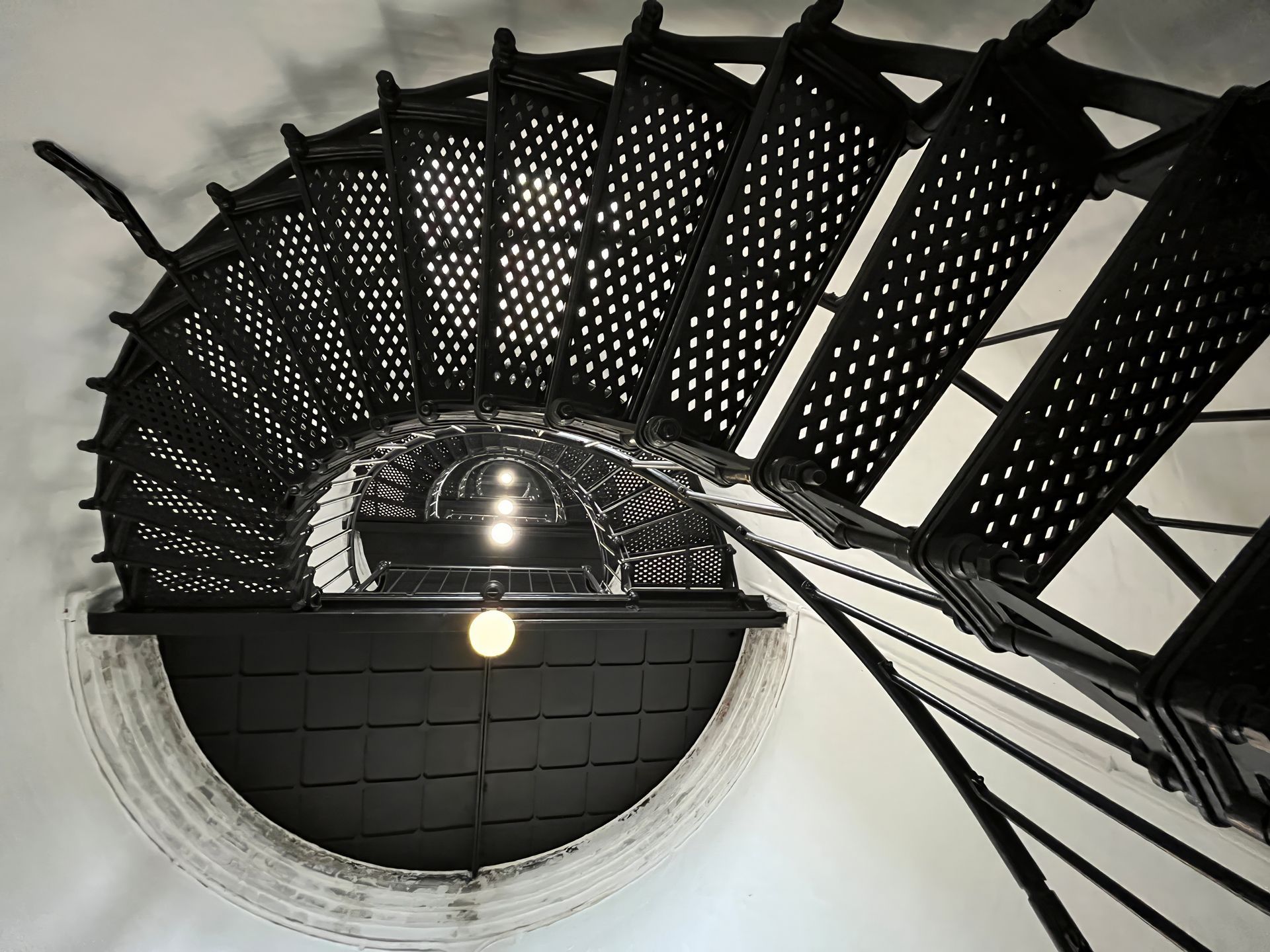 Black spiral staircase viewed from below around a circular white shaft and dark ceiling.