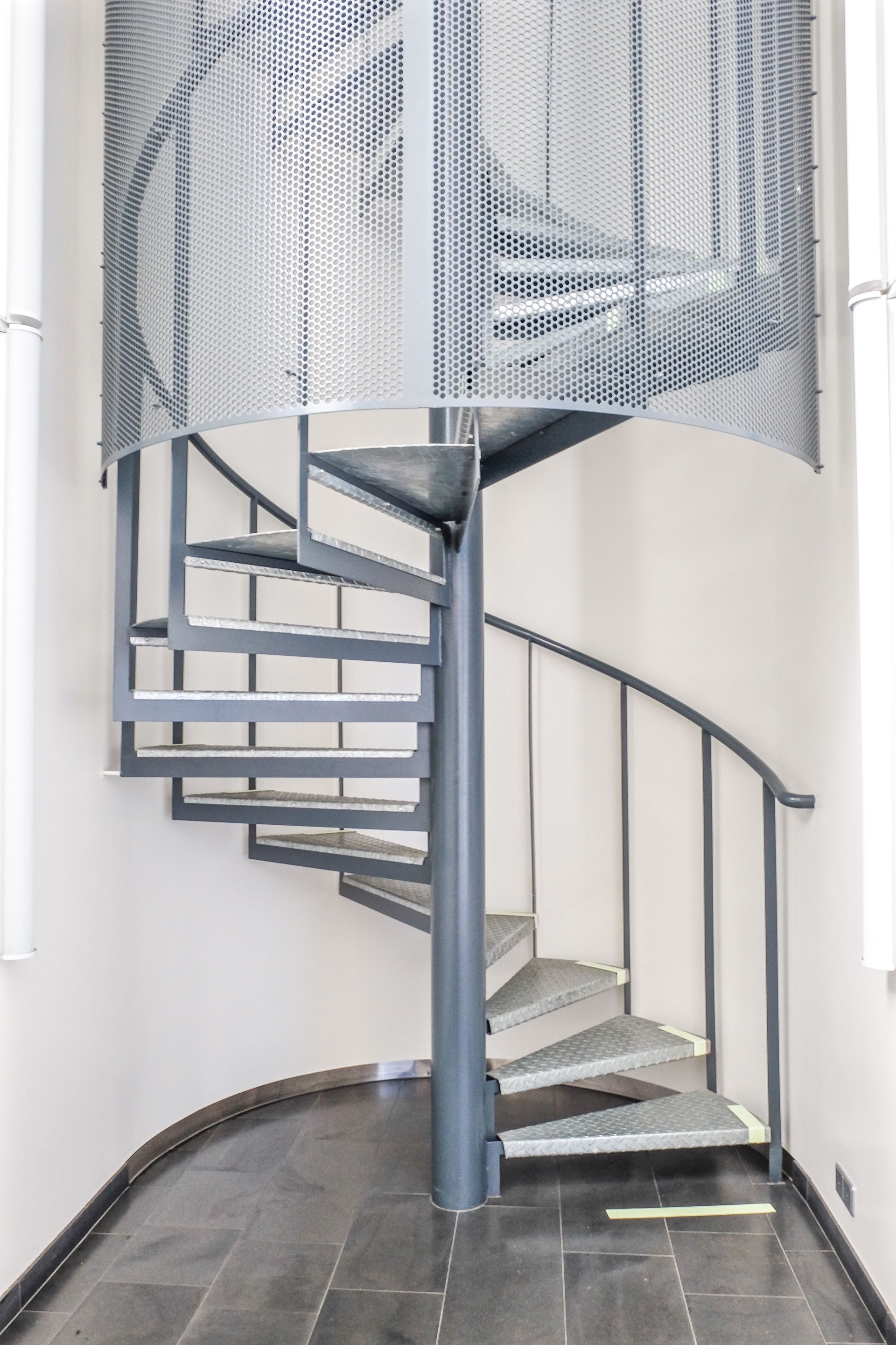 Spiral staircase with gray metal steps and railing in a white interior space