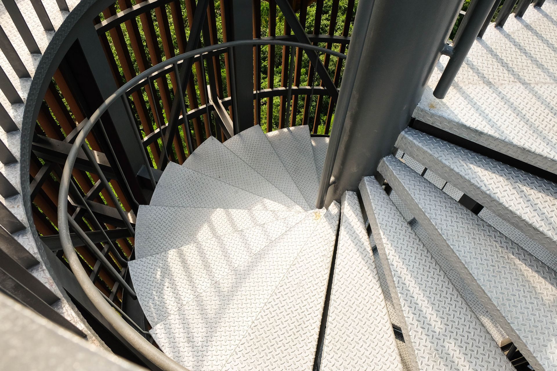 Spiral metal staircase with black railing and white steps, viewed from above.