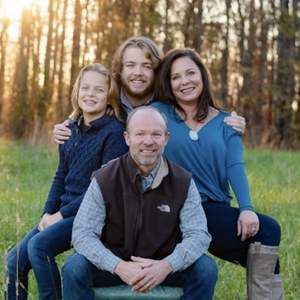 A family is posing for a picture while sitting on a bench in a field.
