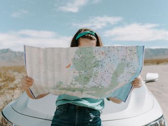 A woman is standing next to a car holding a map.