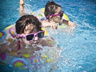 Two young girls wearing sunglasses are swimming in a pool.