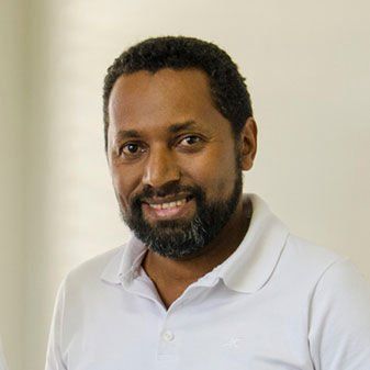 Um homem com barba está vestindo uma camisa pólo branca e sorrindo.