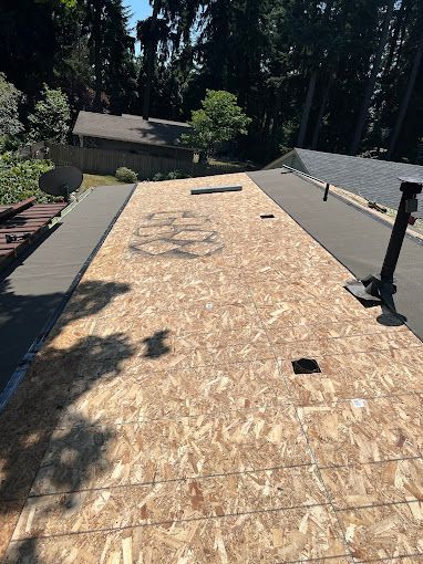 A roof with a lot of plywood on it and a lot of trees in the background.