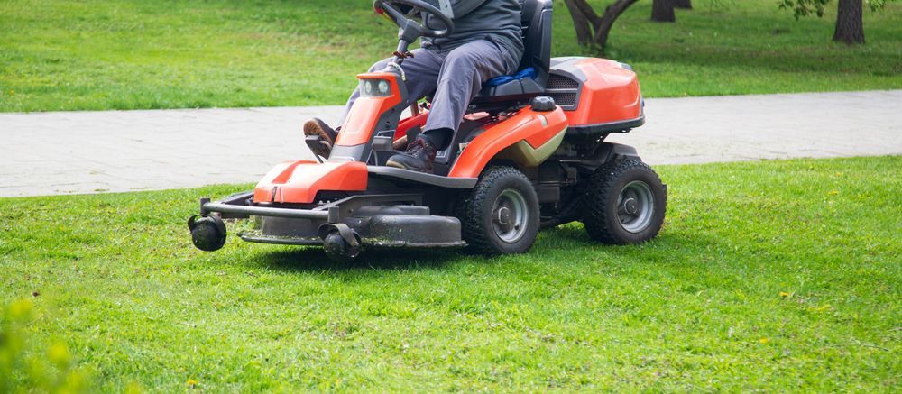 A man is riding a lawn mower in a park.