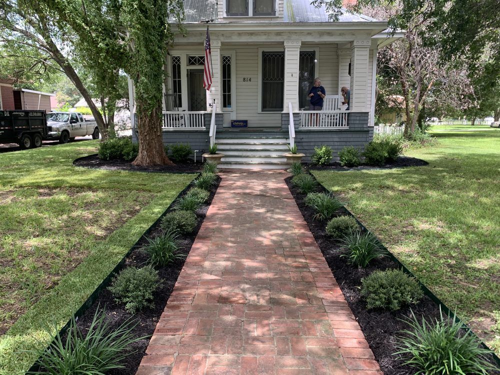 A brick walkway leading to a white house with a porch.