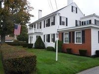 White house with black shutters, red brick addition, and American flag on a manicured lawn