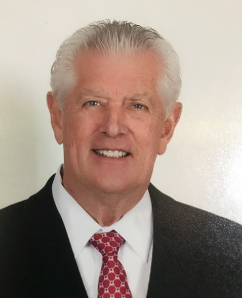 Studio portrait of a smiling man in a black suit, white shirt, and red patterned tie.