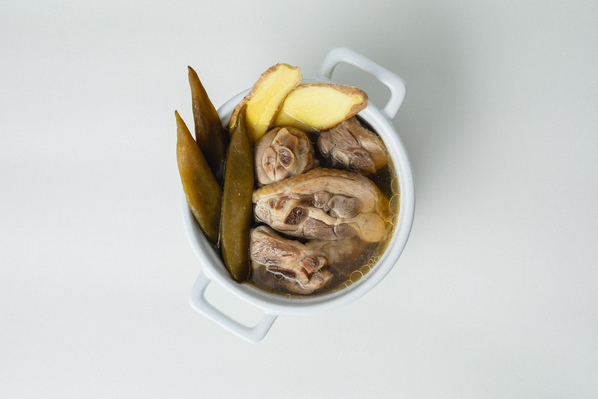 淺色背景上的白色鍋子裡盛著煮熟的肉、馬鈴薯和綠色蔬菜