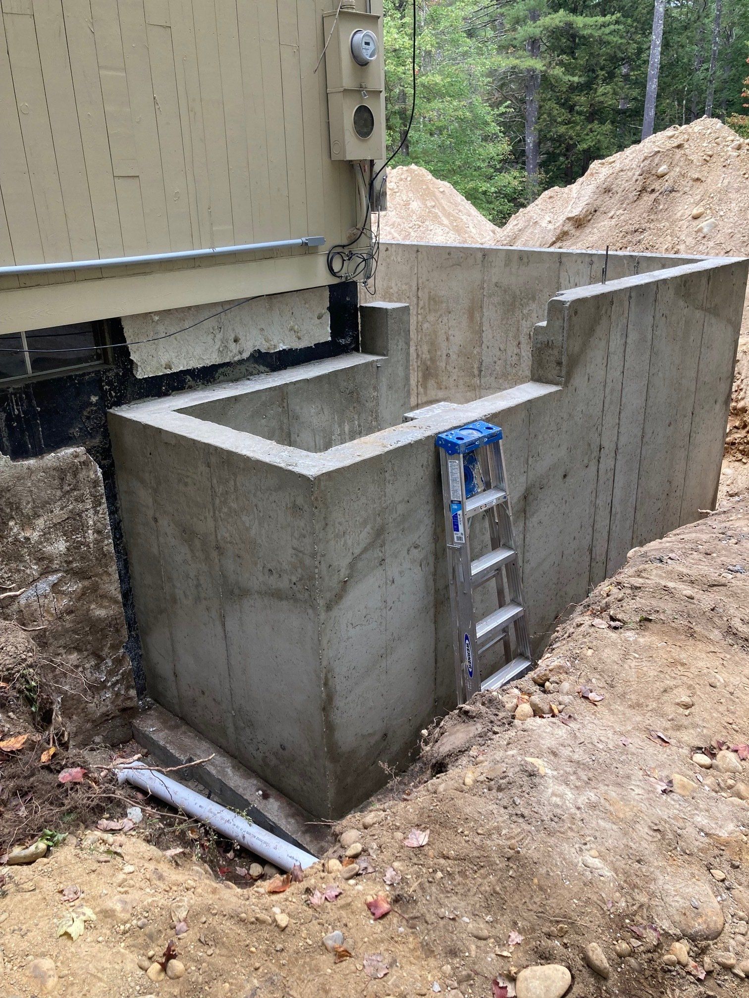 A ladder is sitting in the dirt next to a concrete wall.