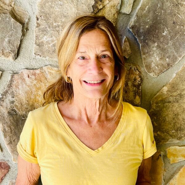 Woman in yellow shirt smiles in front of a stone wall.