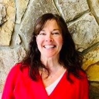 Woman in red sweater smiles in front of a stone wall.