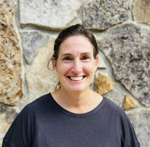 Woman smiling in front of a stone wall, wearing a dark gray shirt.