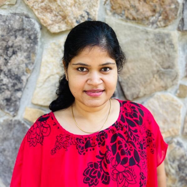 Woman in a red patterned top smiling in front of a stone wall.