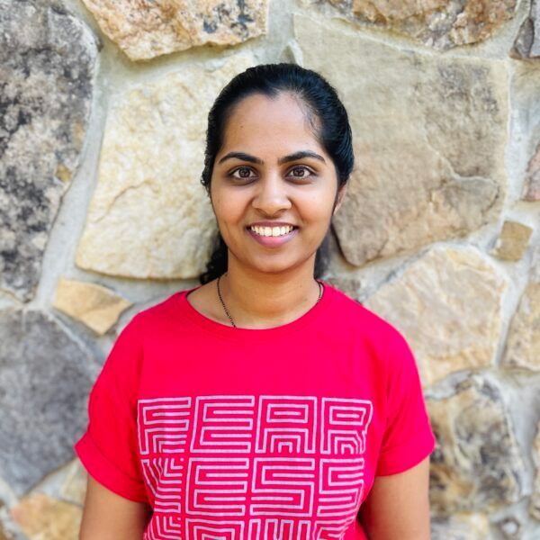 Woman wearing a red shirt with white text smiles in front of a stone wall.