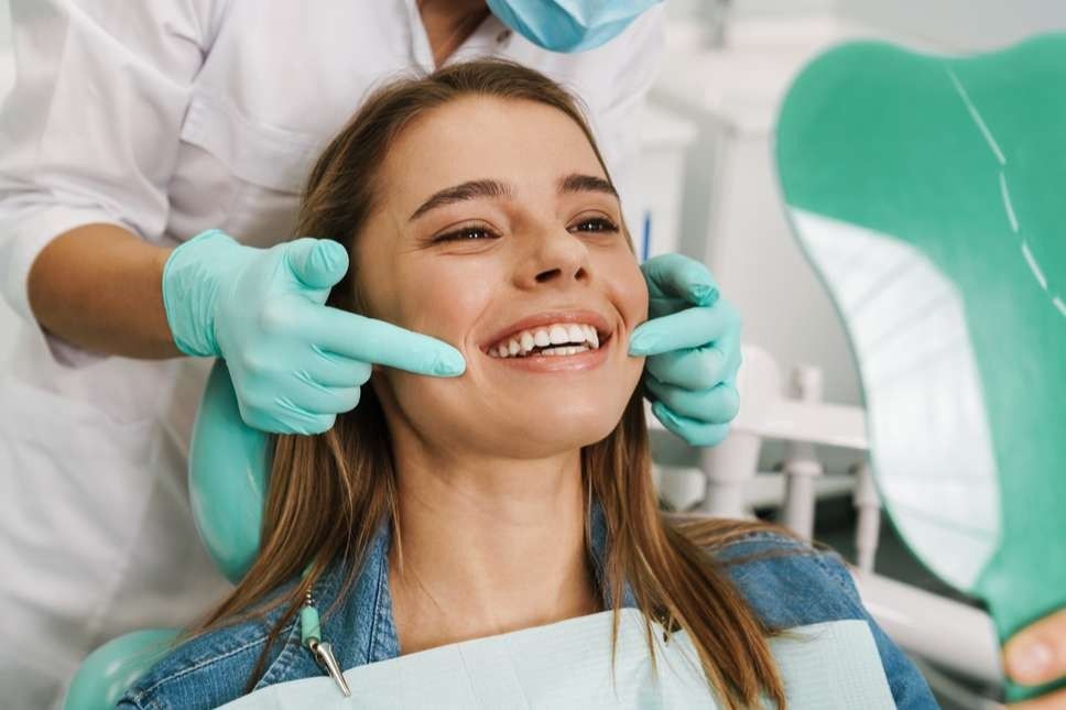 Dentist examining a patient's smile in dental chair, holding a mirror.