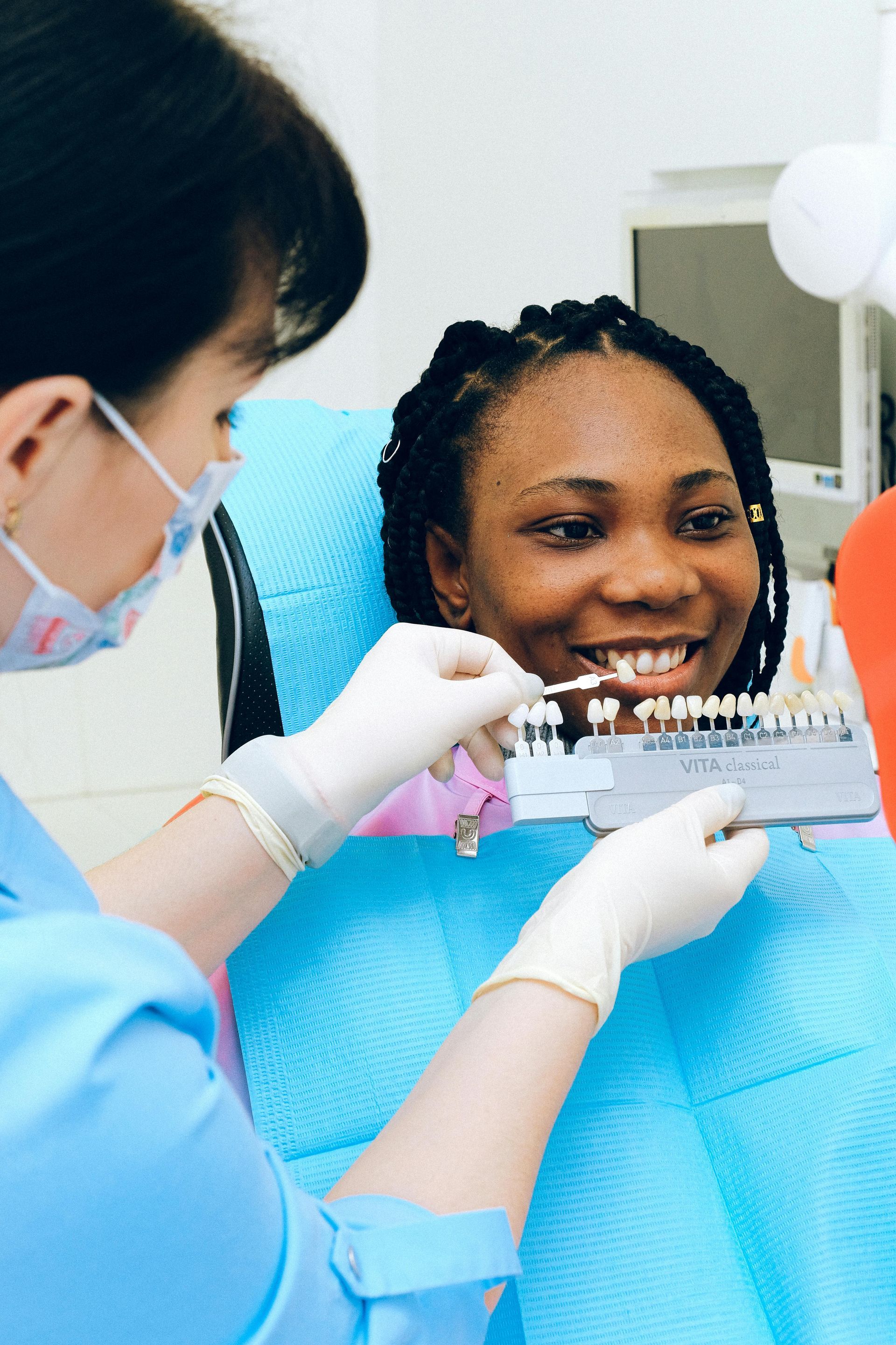 Dentist with gloves holding shade guide near a patient's teeth in a dental office.