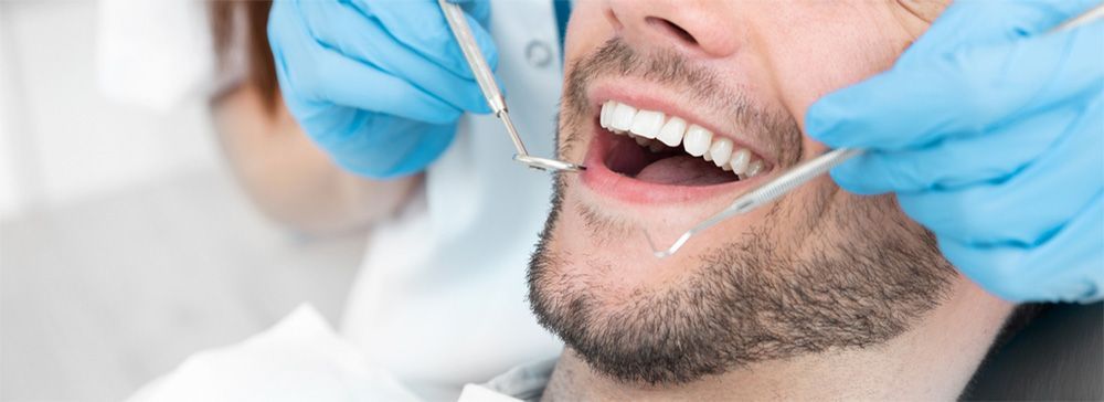 A dentist examining a patient's open mouth with dental tools.