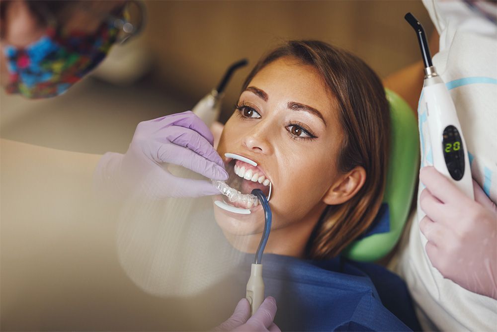 Woman in dental chair, mouth open for treatment. Dentist using curing light.