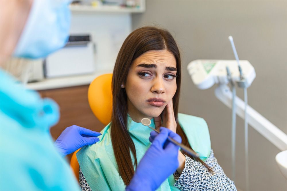 Woman in dentist chair looking distressed as dentist examines her mouth.
