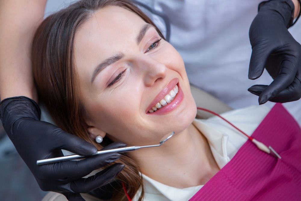 Woman in dental chair, smiling; dentist holding tools.
