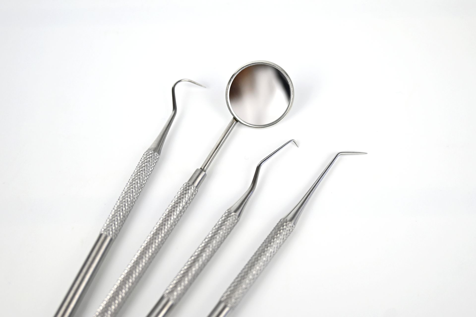 Four silver dental tools, including a mirror, arranged on a white background