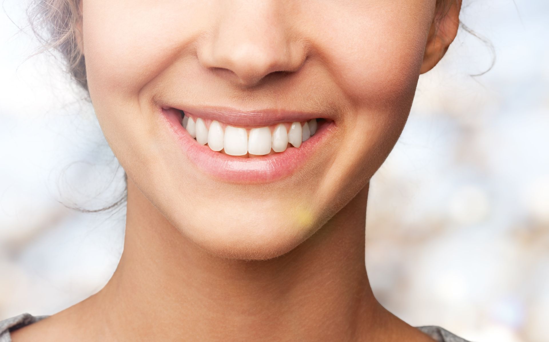 Close-up of a smiling mouth and lower face with white teeth against a light background