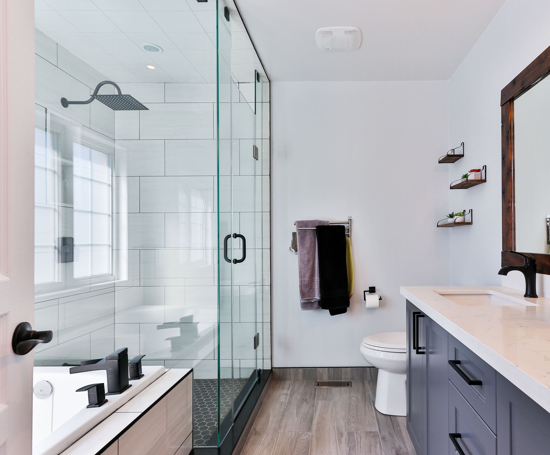 Modern bathroom with glass shower, white walls, gray cabinets, and wooden accents.