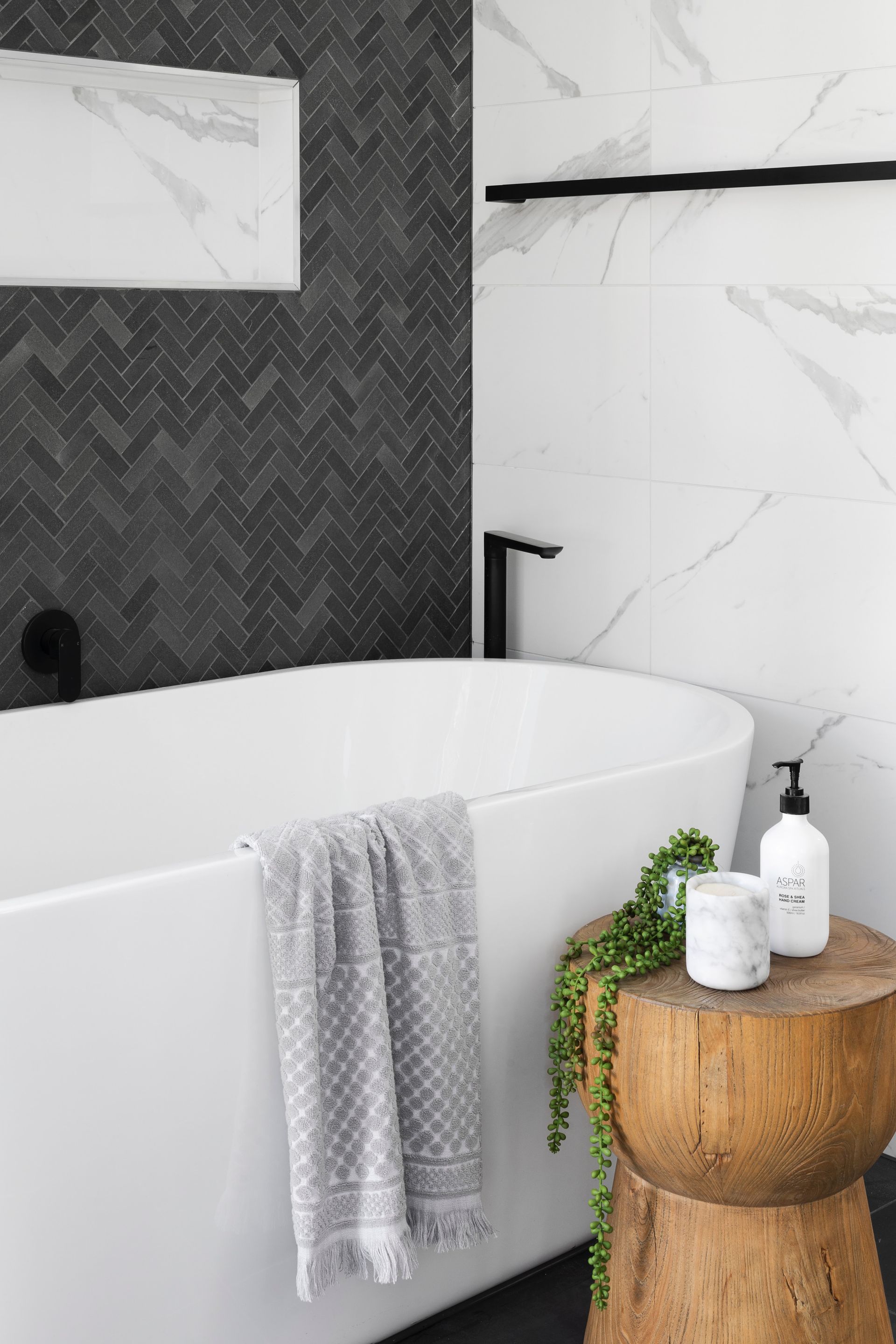 Modern bathroom with white tub, black fixtures, and wood accent table.