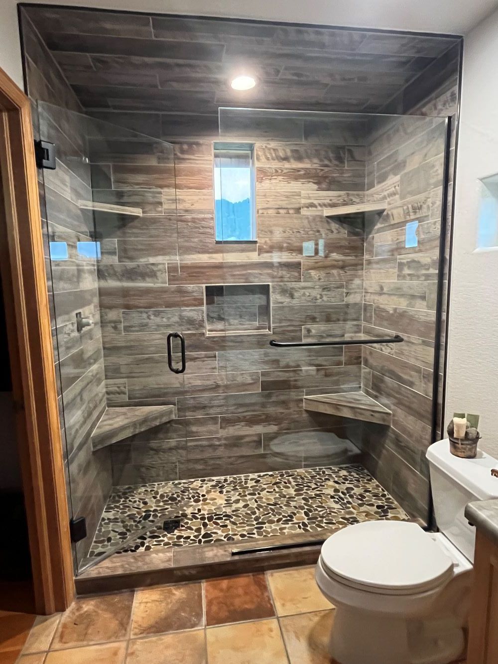 Walk-in shower with wood-look tile, glass doors, pebble floor, and built-in benches.