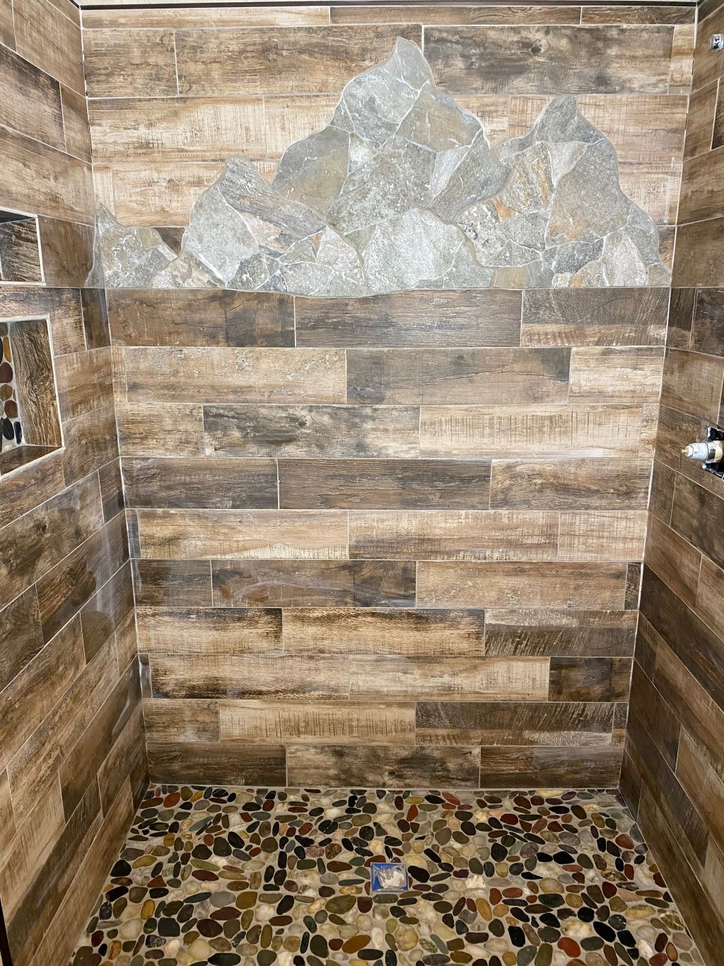Shower with wood-look tile walls, a stone mountain accent, and a pebble floor.