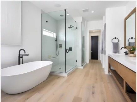 Modern, white bathroom with a freestanding tub, glass shower, wooden vanity, and light wood floors.