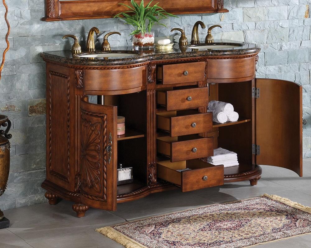 Double vanity with dark granite countertop, carved wooden cabinets, open drawers, and sinks with bronze faucets.