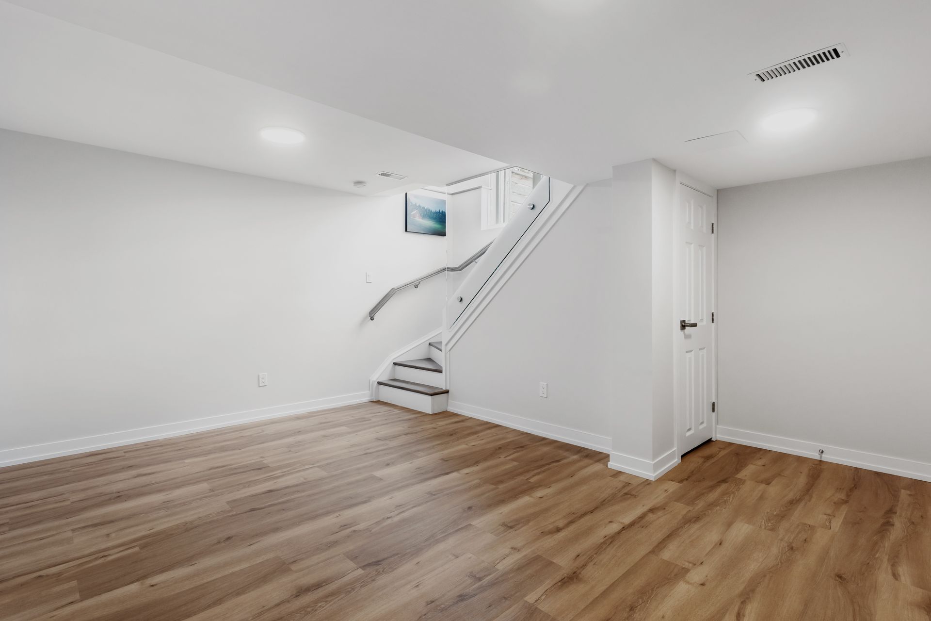 Empty room with wooden floors, white walls, and stairs leading upwards.