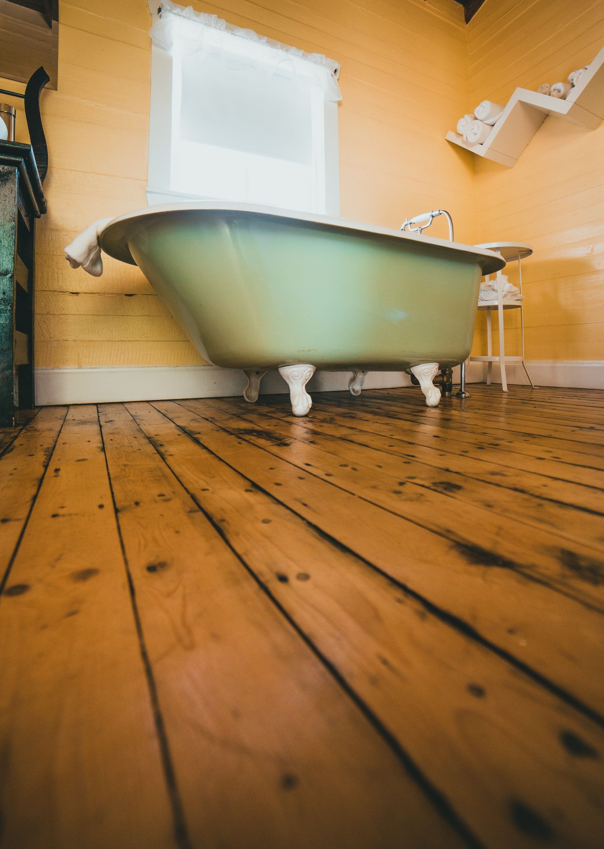 Green clawfoot bathtub in a room with wood floors and yellow walls.