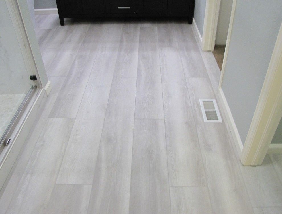 Light gray wood-look flooring in a bathroom hallway. A dark cabinet is in the background. A vent is in the floor.