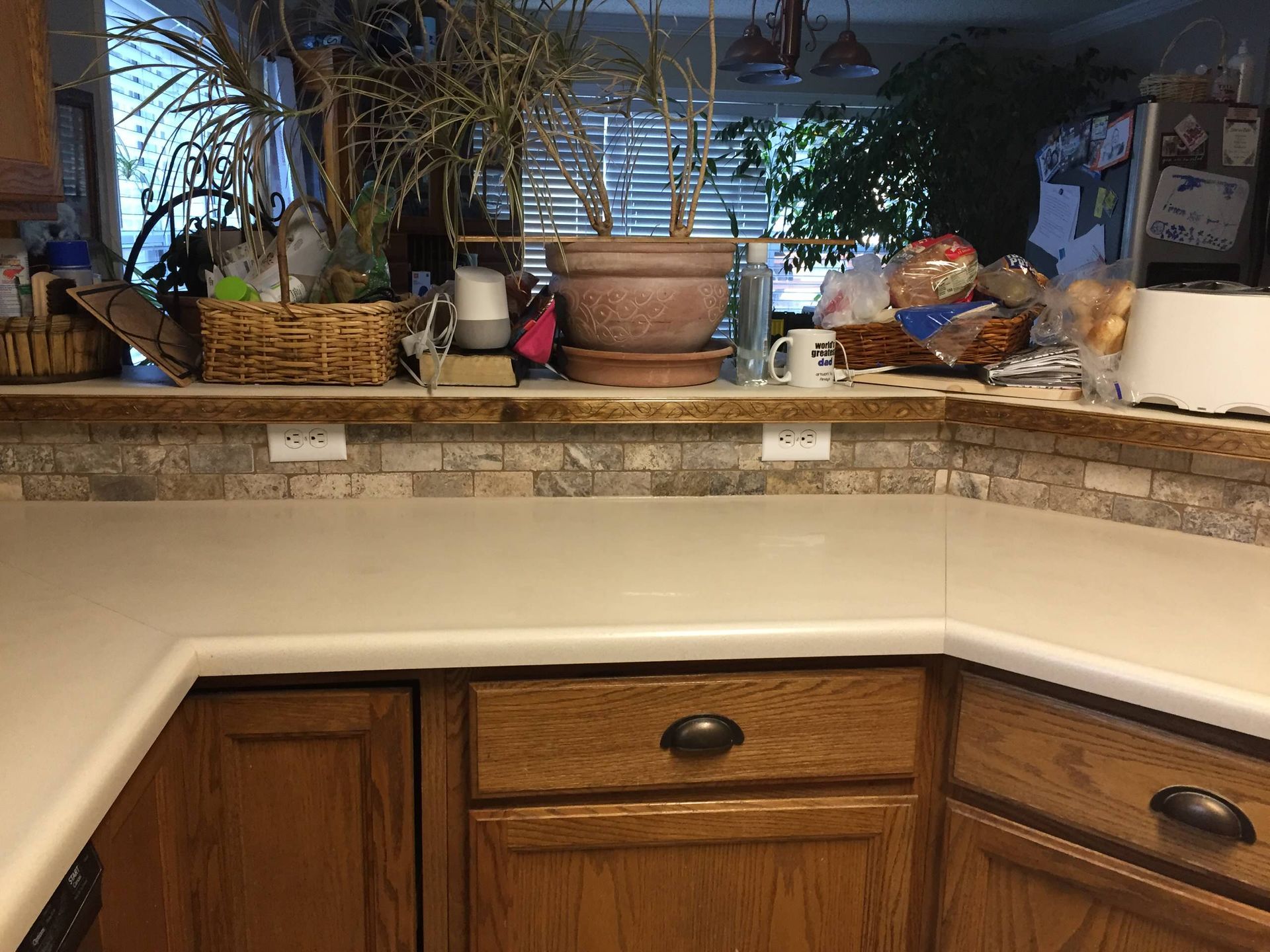 Kitchen countertop with backsplash, cabinets, and various objects on the counter.