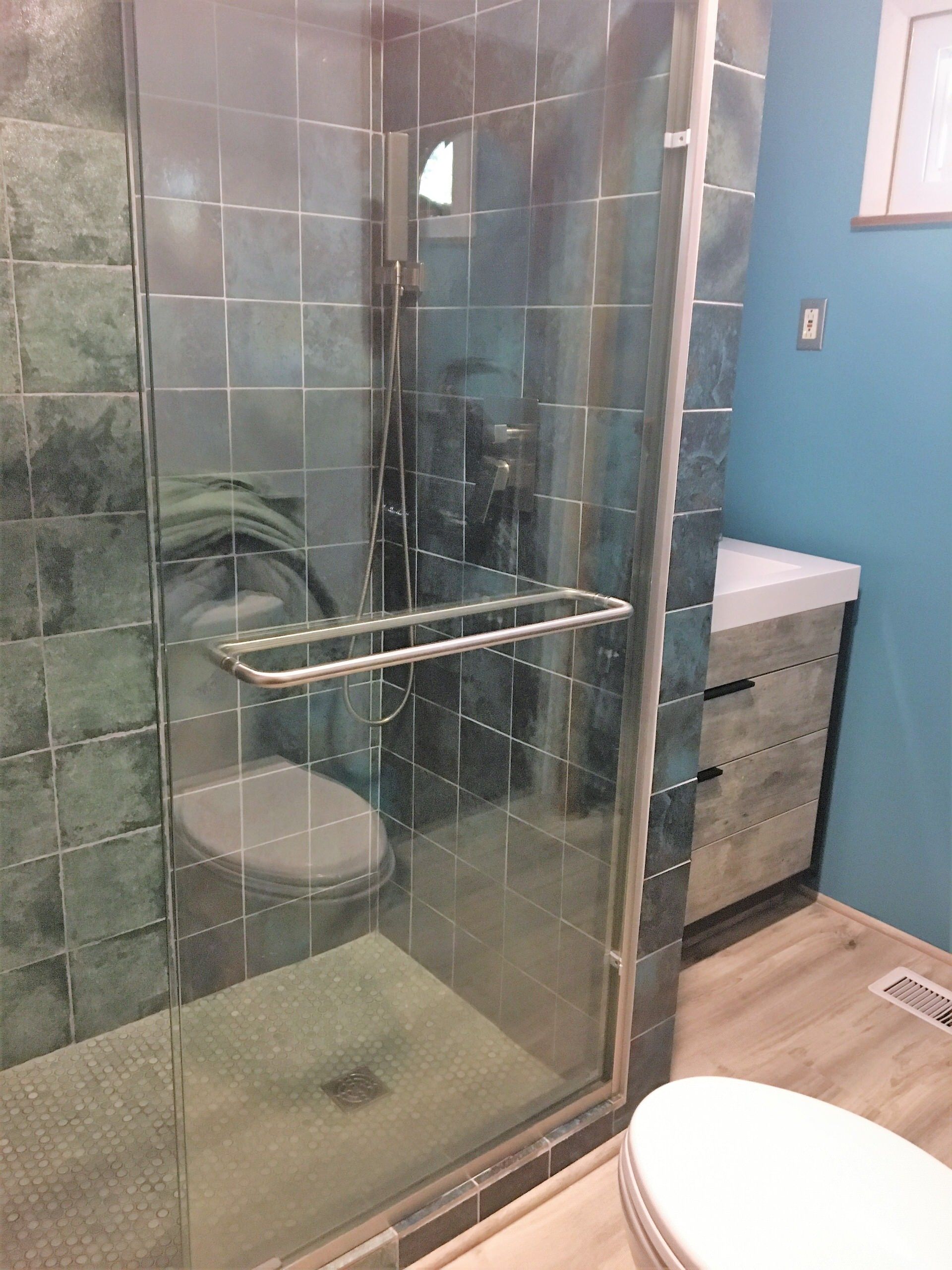 Bathroom with a glass shower, toilet, and vanity. Teal tile and blue wall.