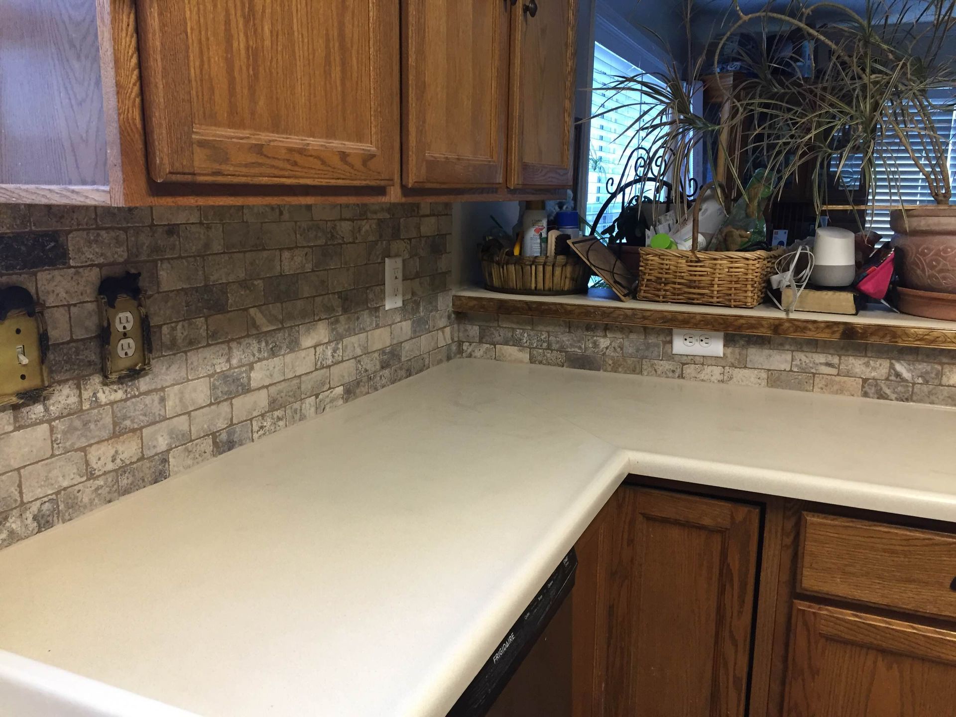 Kitchen with light countertops, brick backsplash, and wooden cabinets.