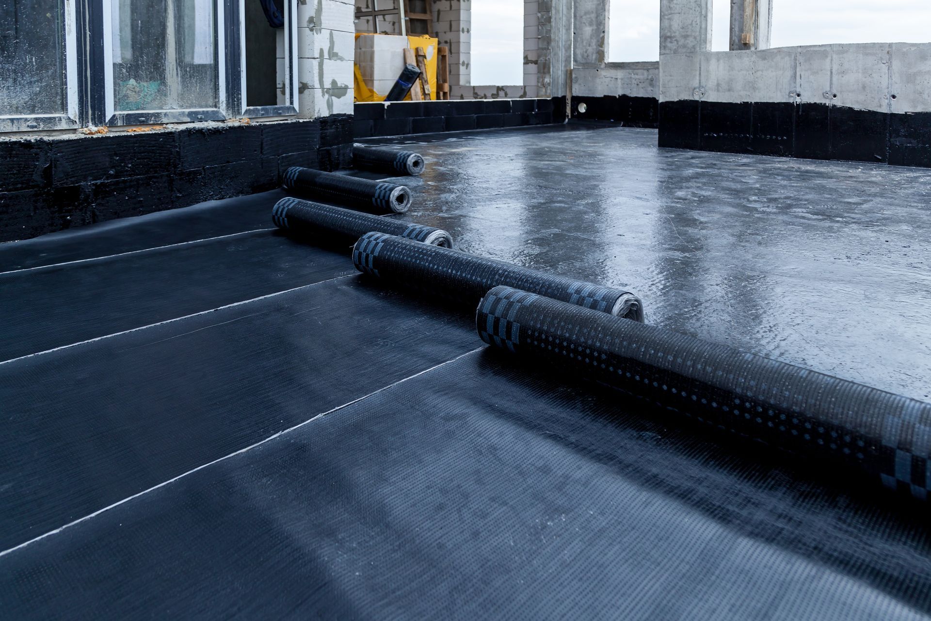 Black rolled waterproofing membrane on a rooftop, with rolls lined up.