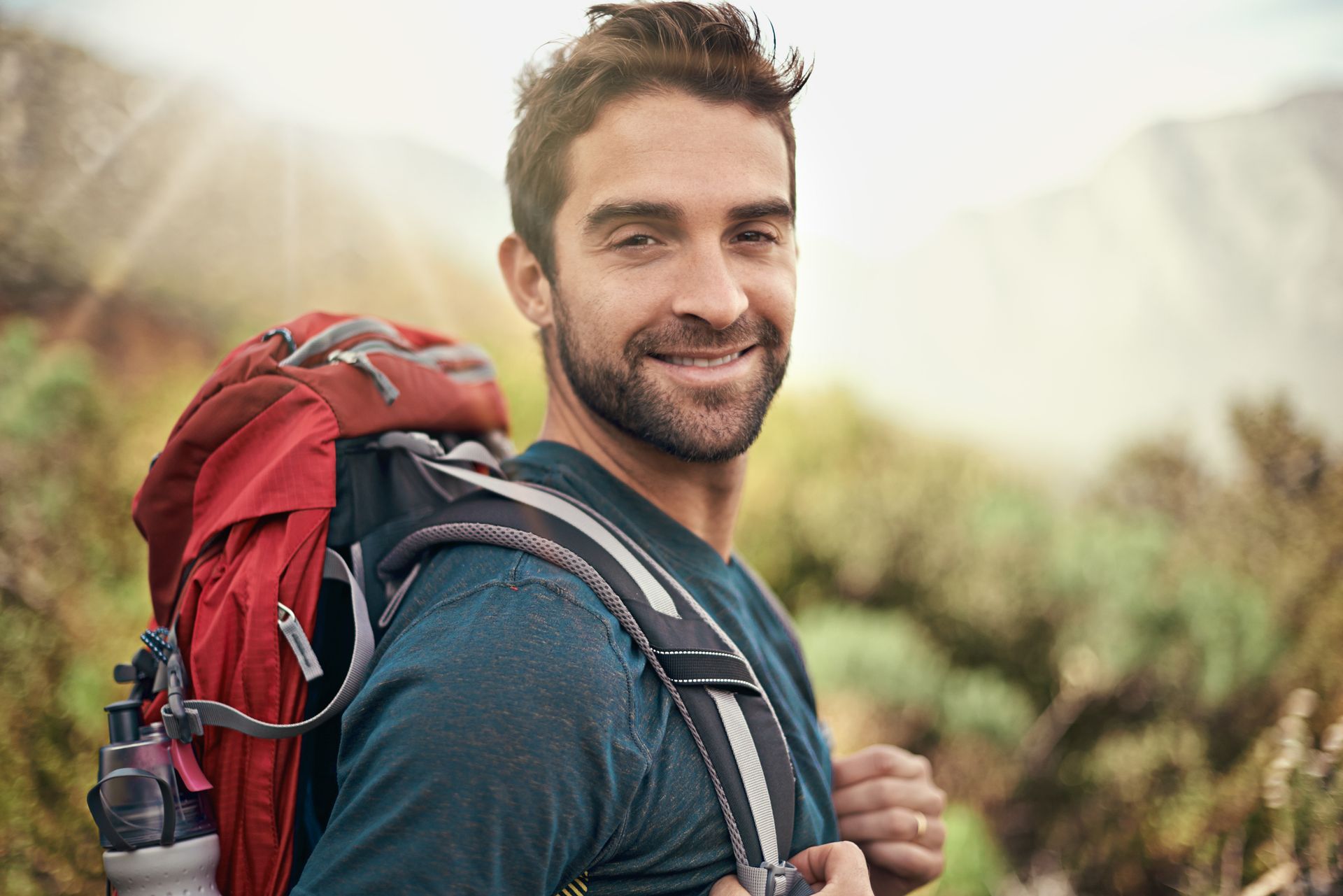 Man with backpack smiles while hiking in the mountains.
