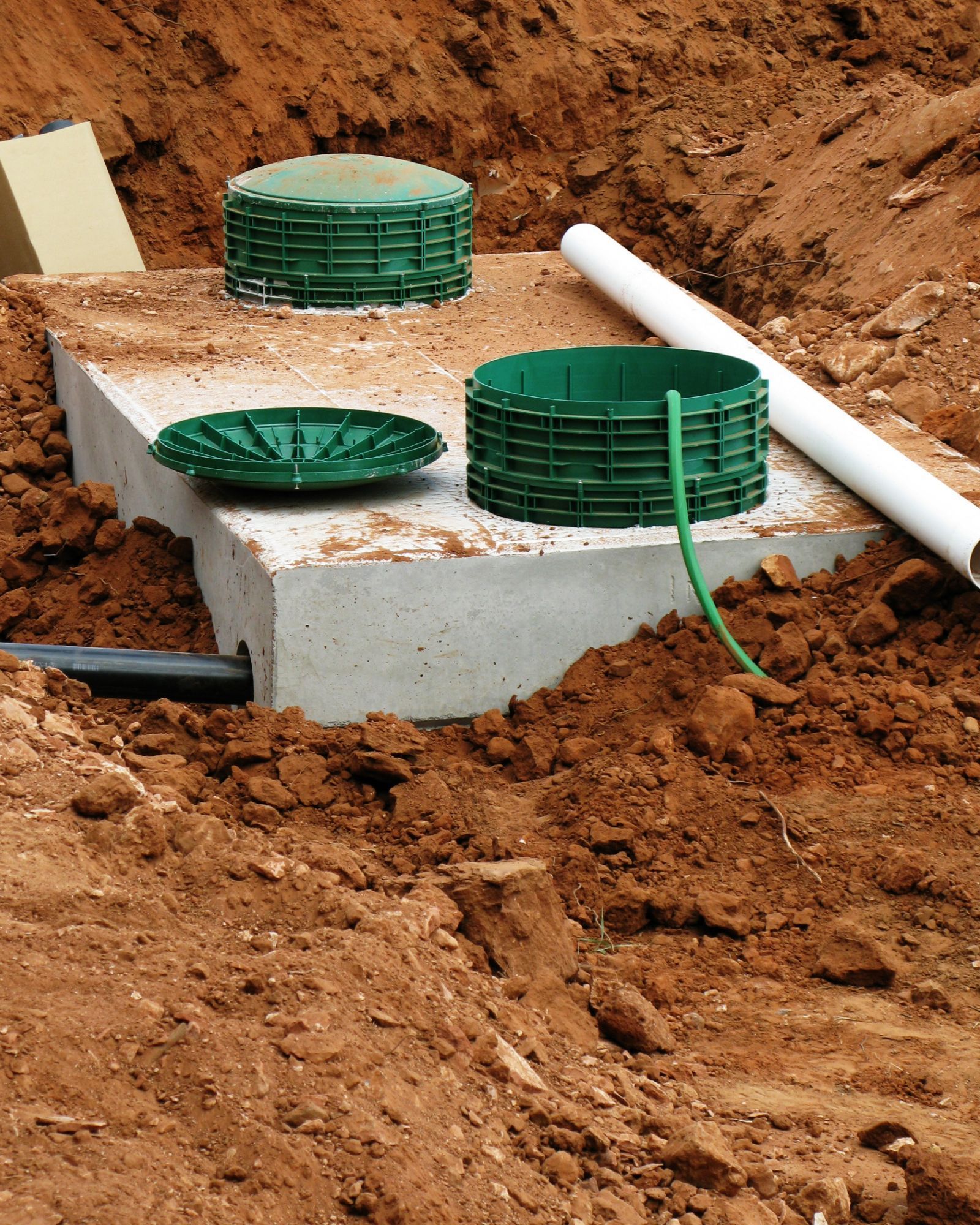Concrete septic tank with green covers and pipes in a dirt excavation. Concrete septic tank with green covers and pipes in a dirt excavation.