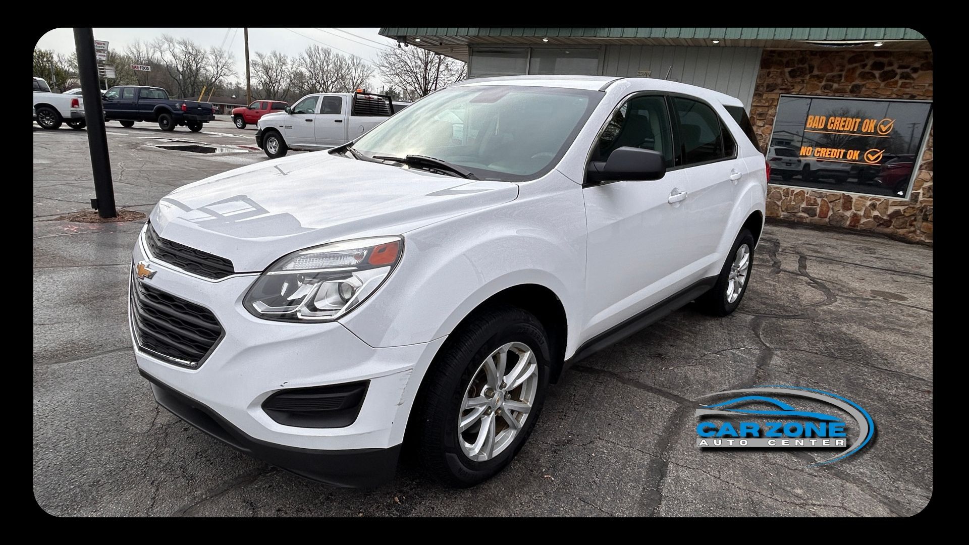 White SUV parked on a wet lot near a building, angled front-left view