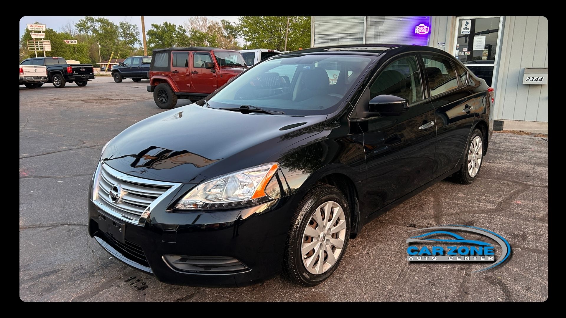 Black sedan parked on a gravel lot outside a building, with a red SUV in the background.