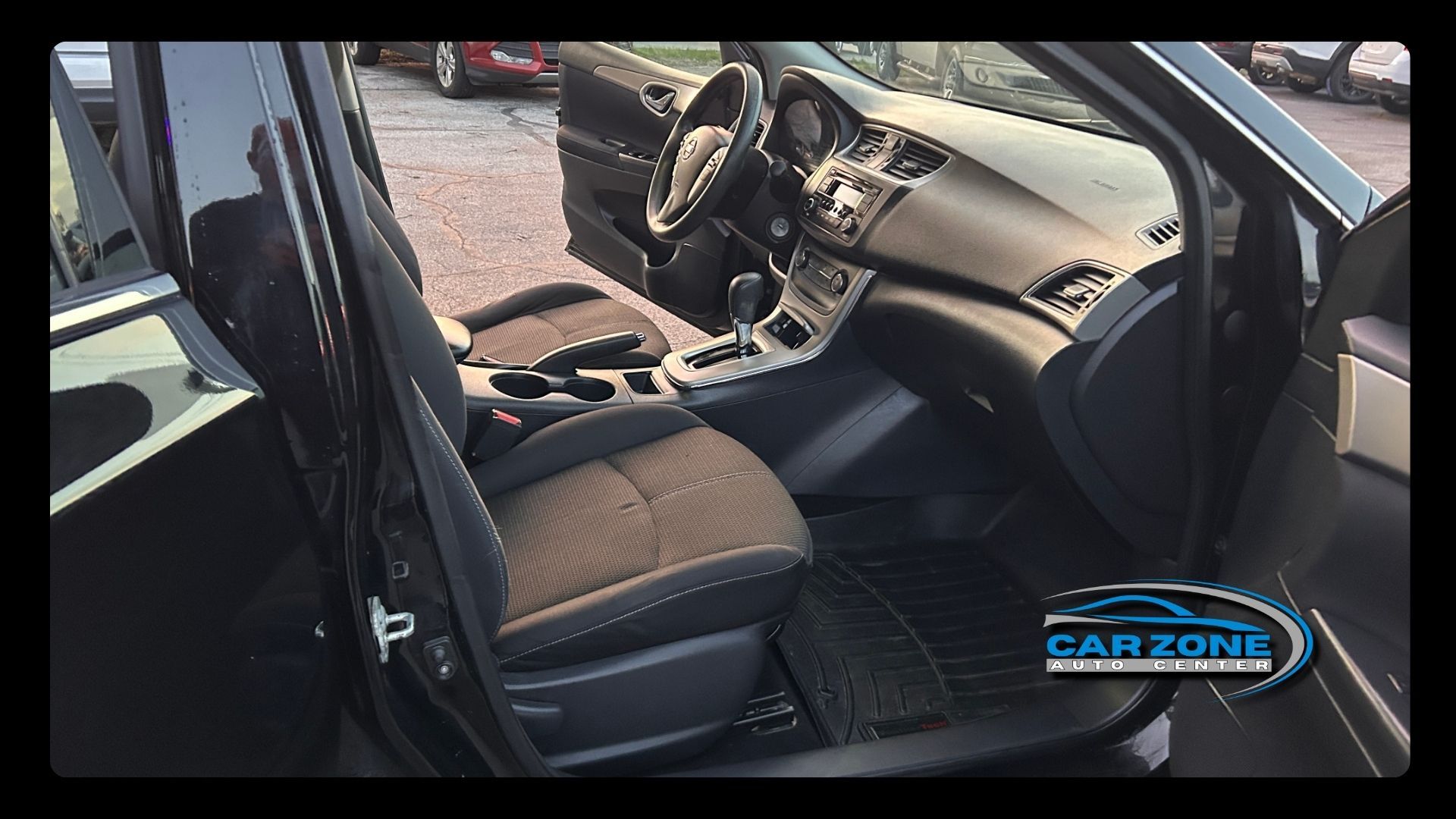 Car interior with black seats, dashboard, center console, and open driver door.
