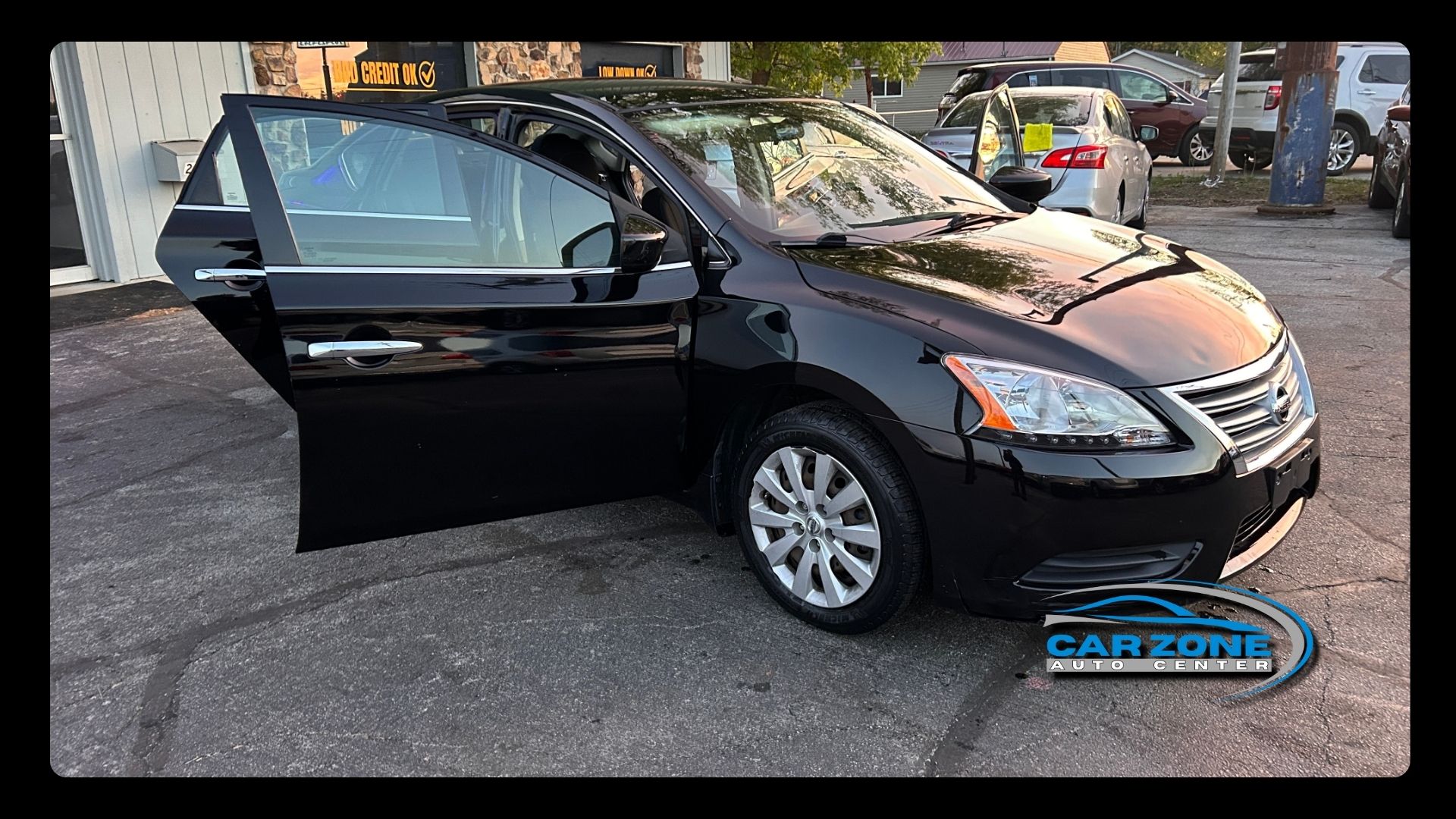 Black sedan with driver door open parked outdoors on a street lot