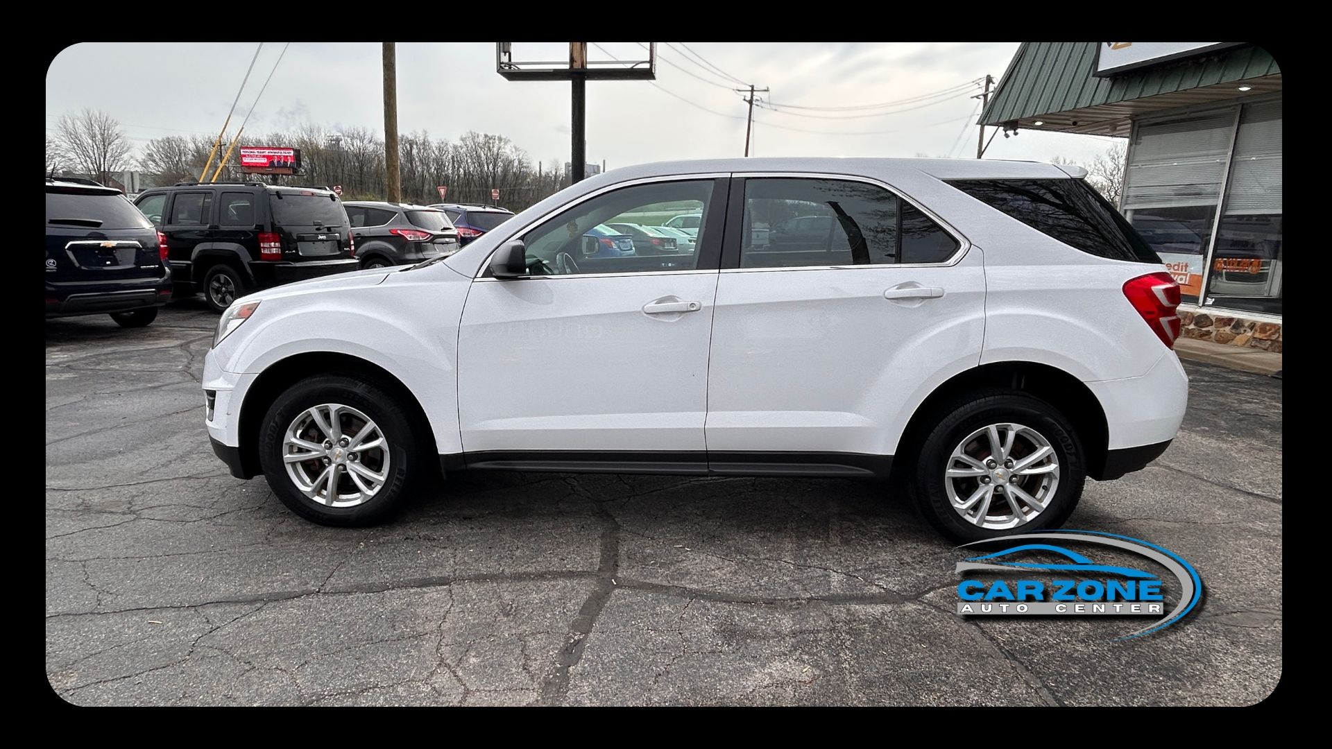 White SUV parked on a wet lot, side view, with other vehicles in the background