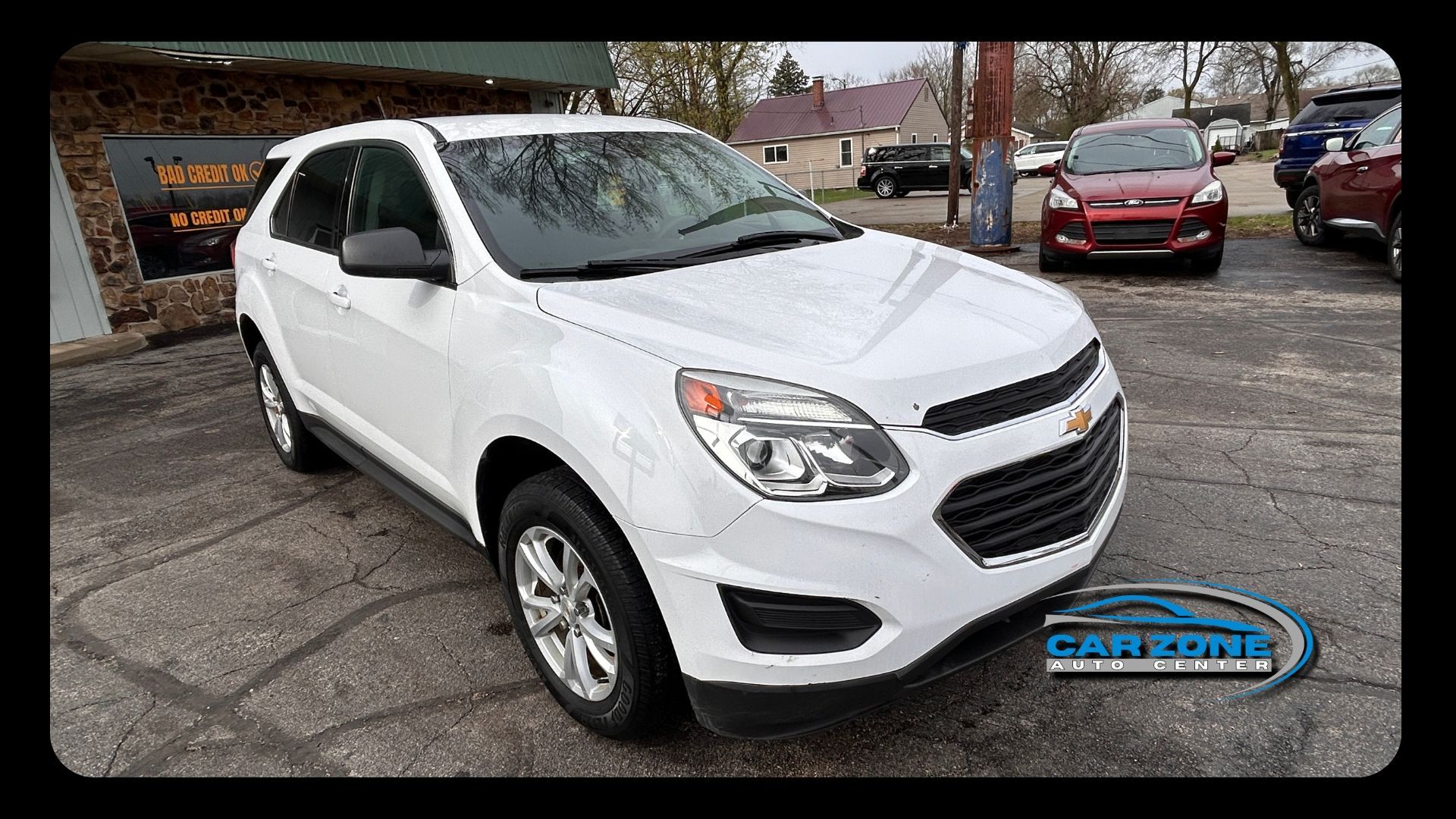 White Chevrolet SUV parked outdoors on a car lot, front-left view with red car in background