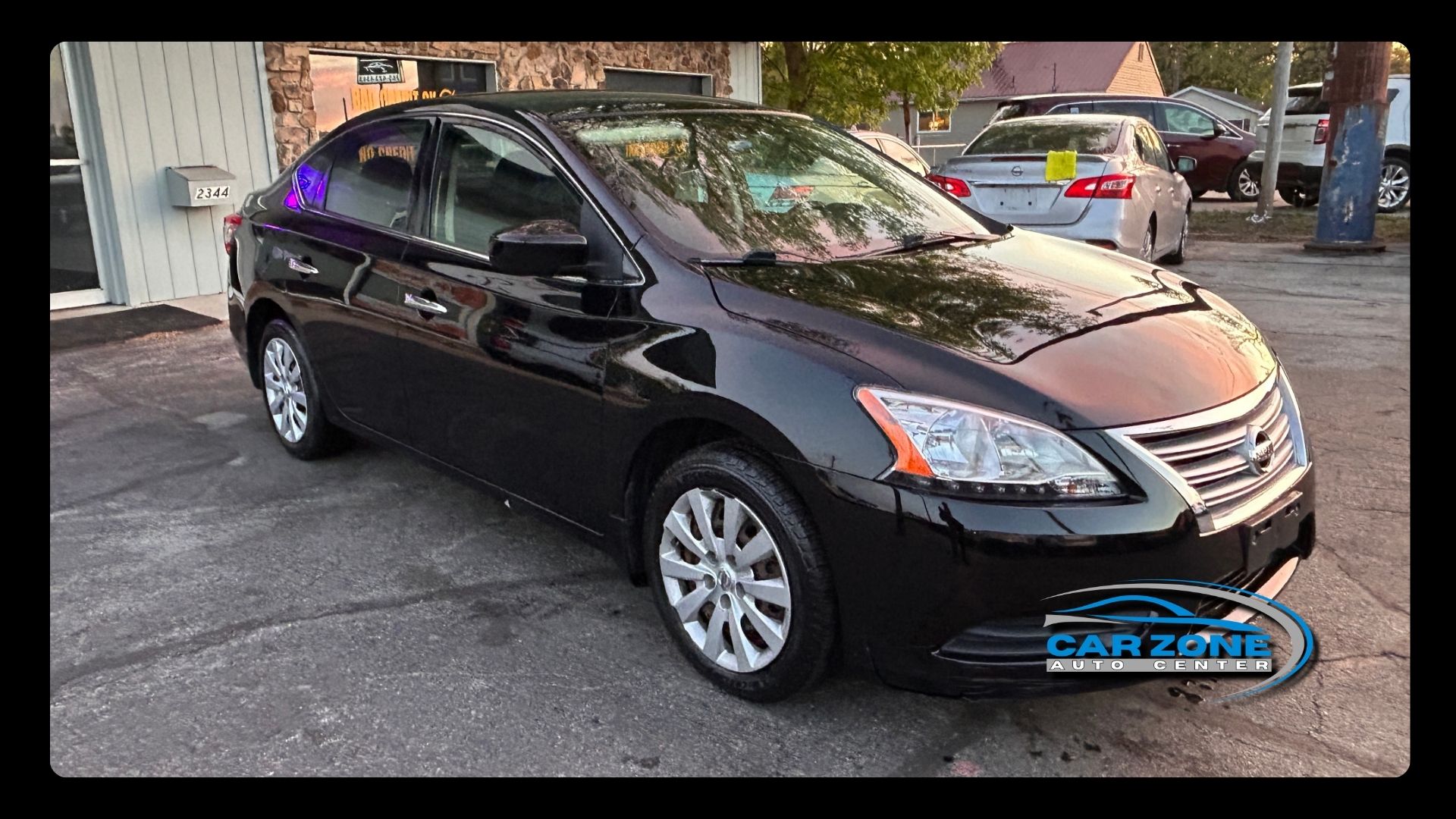 Black sedan parked outdoors under a covered area, shown from the front-left side.