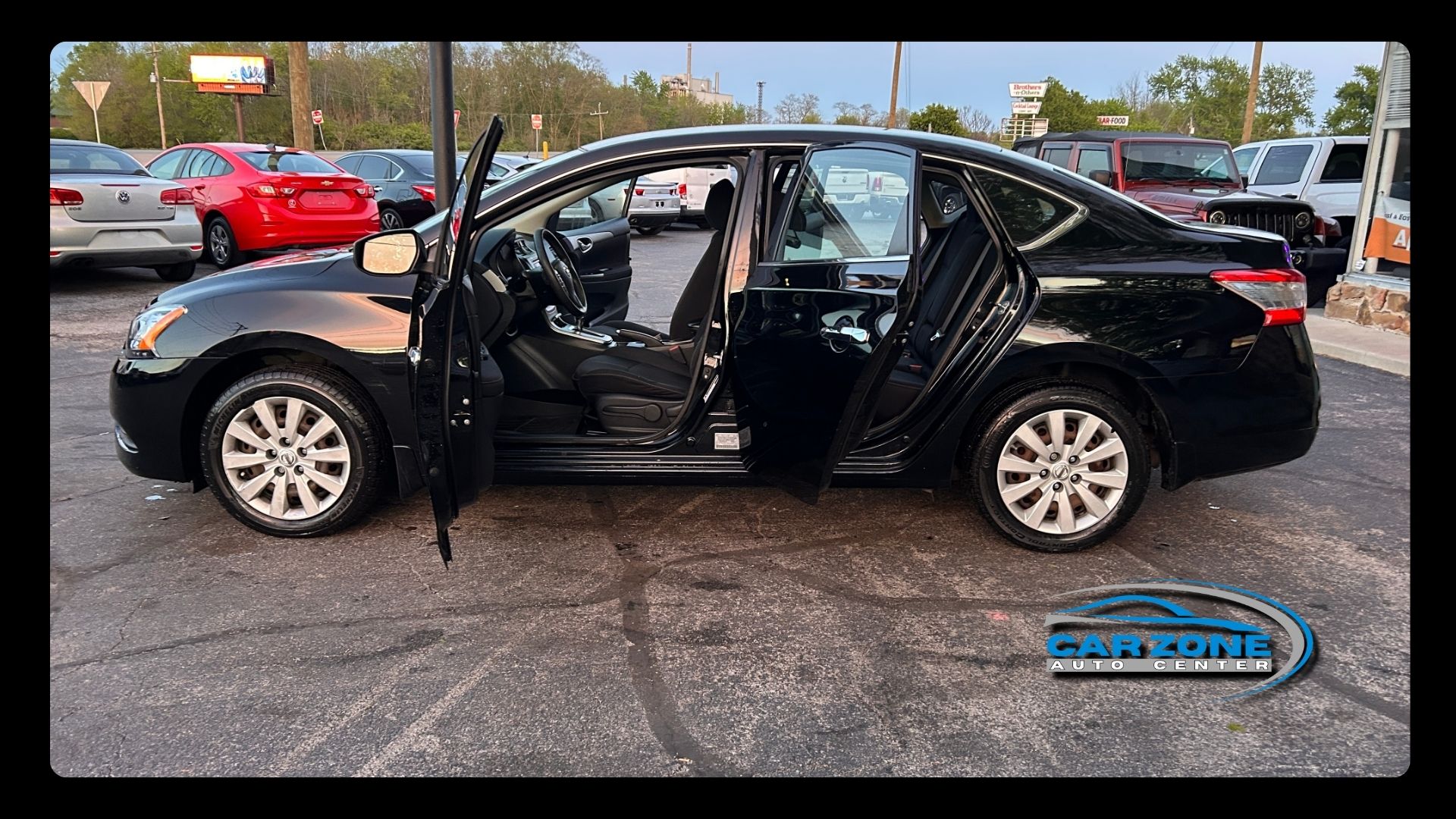 Black sedan with front-left damage and open doors parked in a lot after a crash
